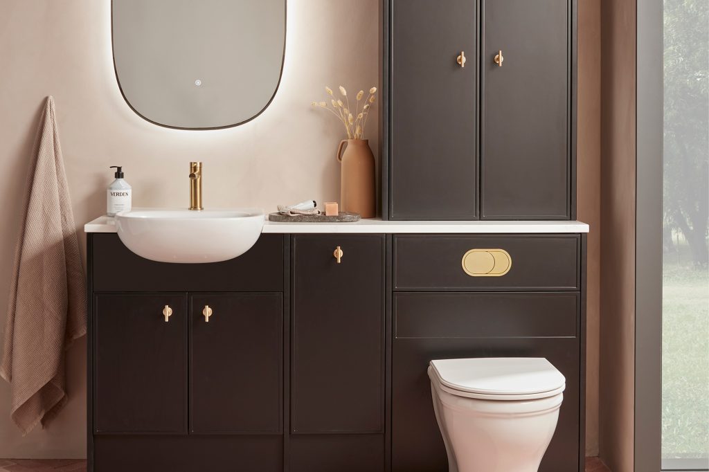Contemporary bathroom featuring dark brown fitted vanity and storage cabinets, white basin, brushed gold fittings, illuminated mirror and concealed toilet cistern