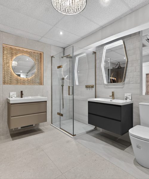 Contemporary bathroom showroom display featuring a glass walk-in shower, floating vanity units, illuminated mirrors and elegant gold fittings