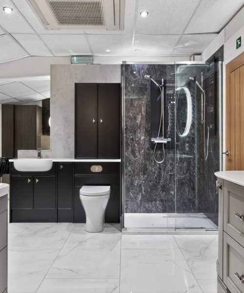 Luxury bathroom showroom display featuring a walk-in glass shower with dark marble-effect wall panels, modern vanity units and white marble-effect flooring